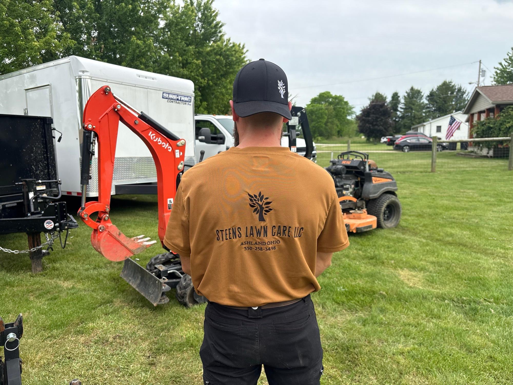 Steen's Lawn Care LLC crew member standing with the company's tractor, mini excavator, and mower