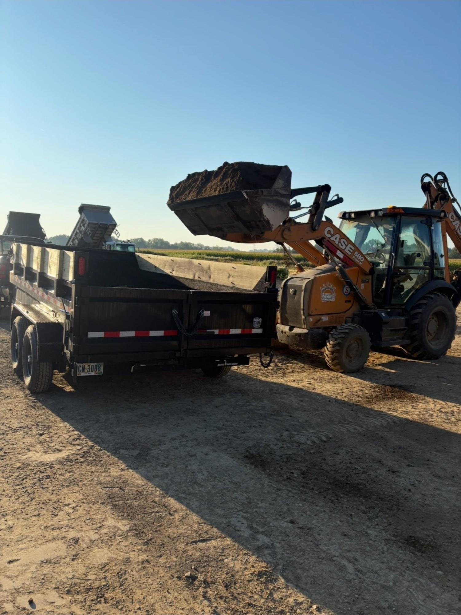 Backhoe loader dumping dirt into a dump trailer during a land clearing job